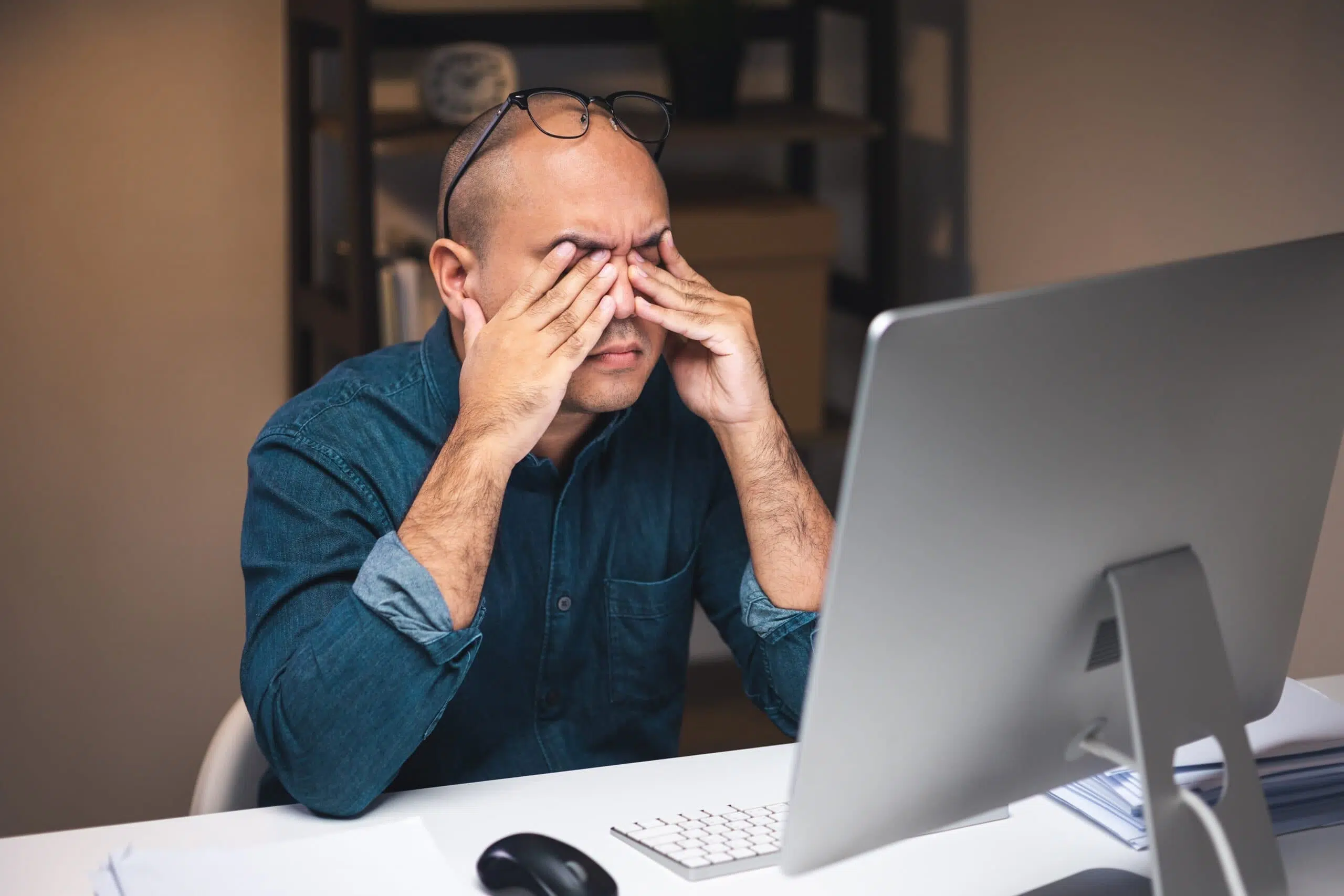 Un homme fatigué et stressé devant un ordinateur à son poste de travail